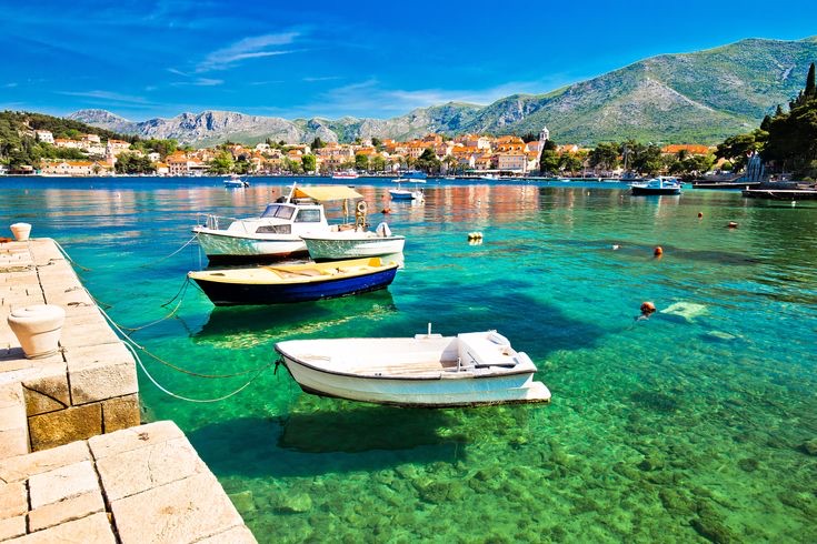 Boats on the crystal-clear water of Cavtat harbour with the old town behind