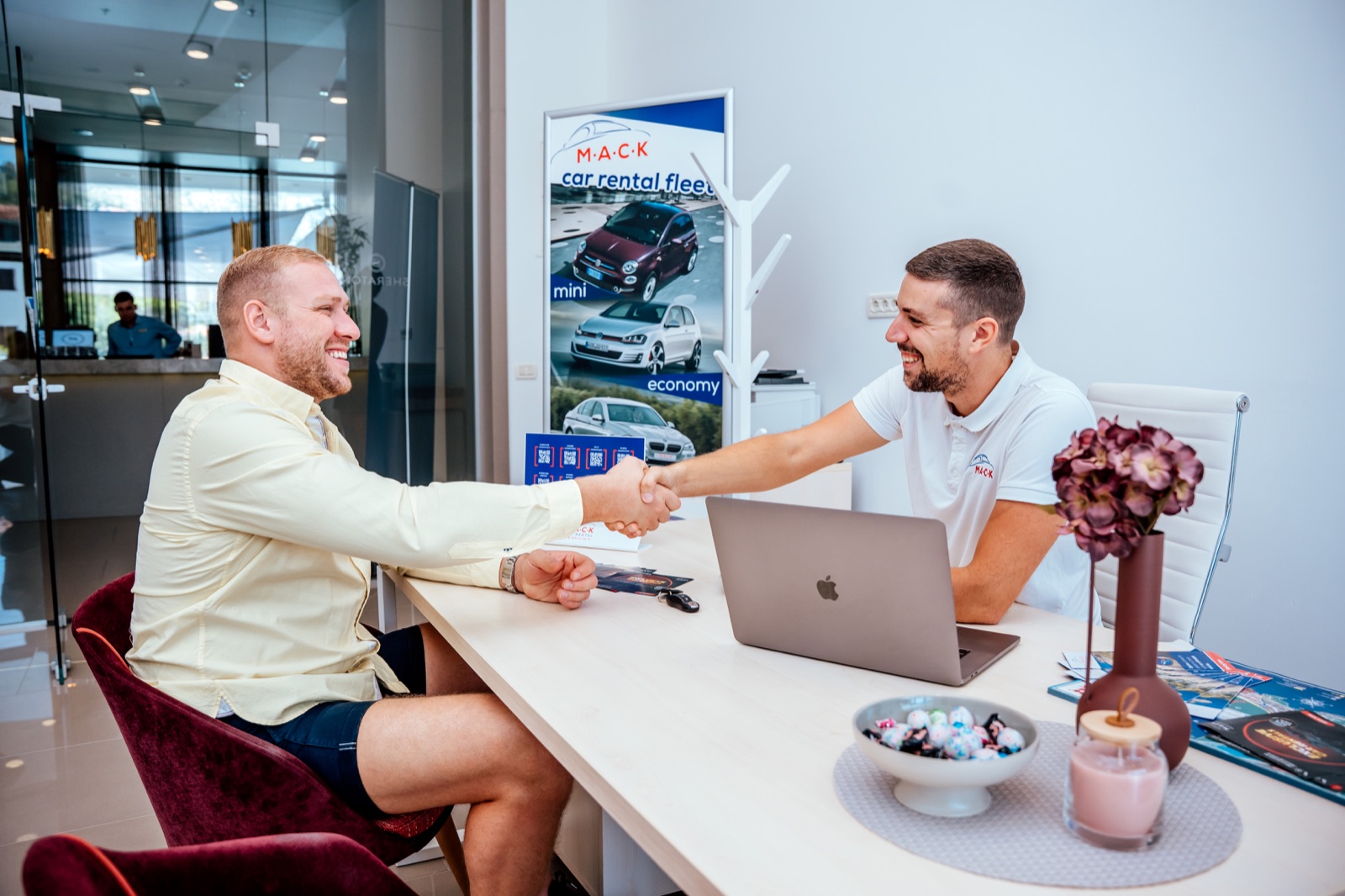 A customer shaking hands with a M.A.C.K. agent across the desk at the rental office