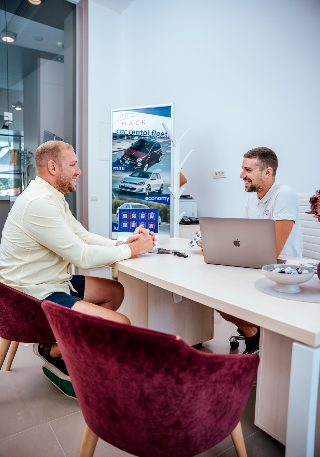 Two people talking across a desk with a laptop at the M.A.C.K. rental office