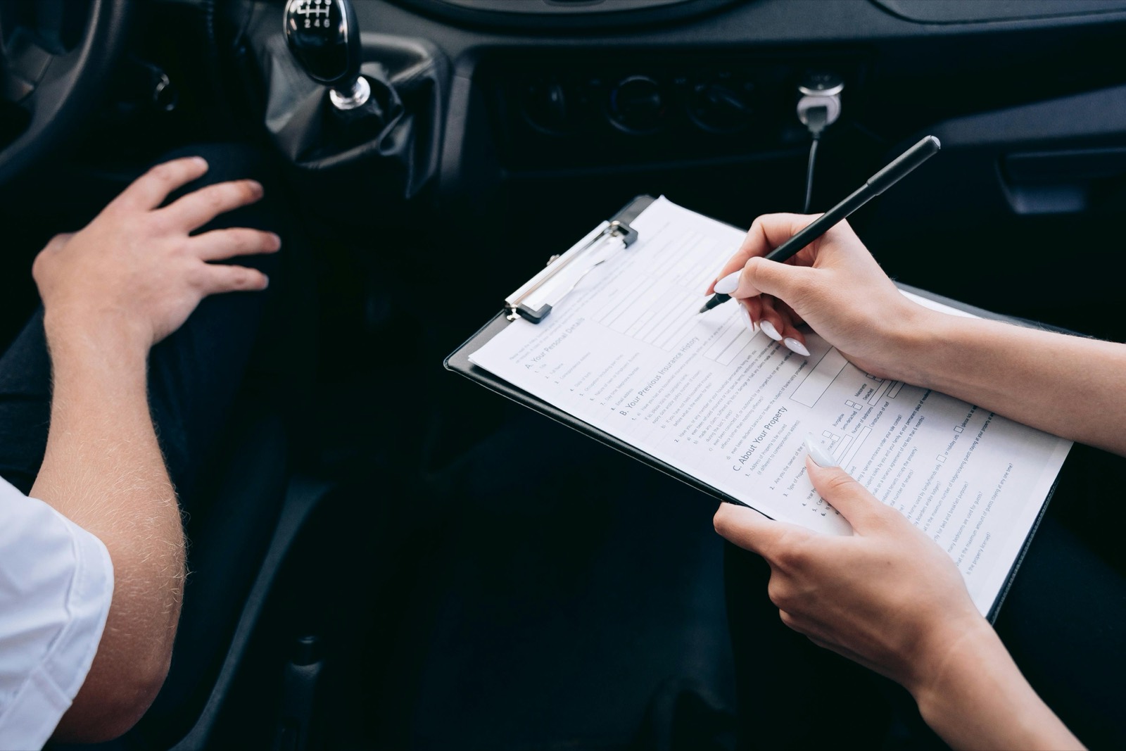 A customer signing a car rental agreement on a clipboard inside the vehicle
