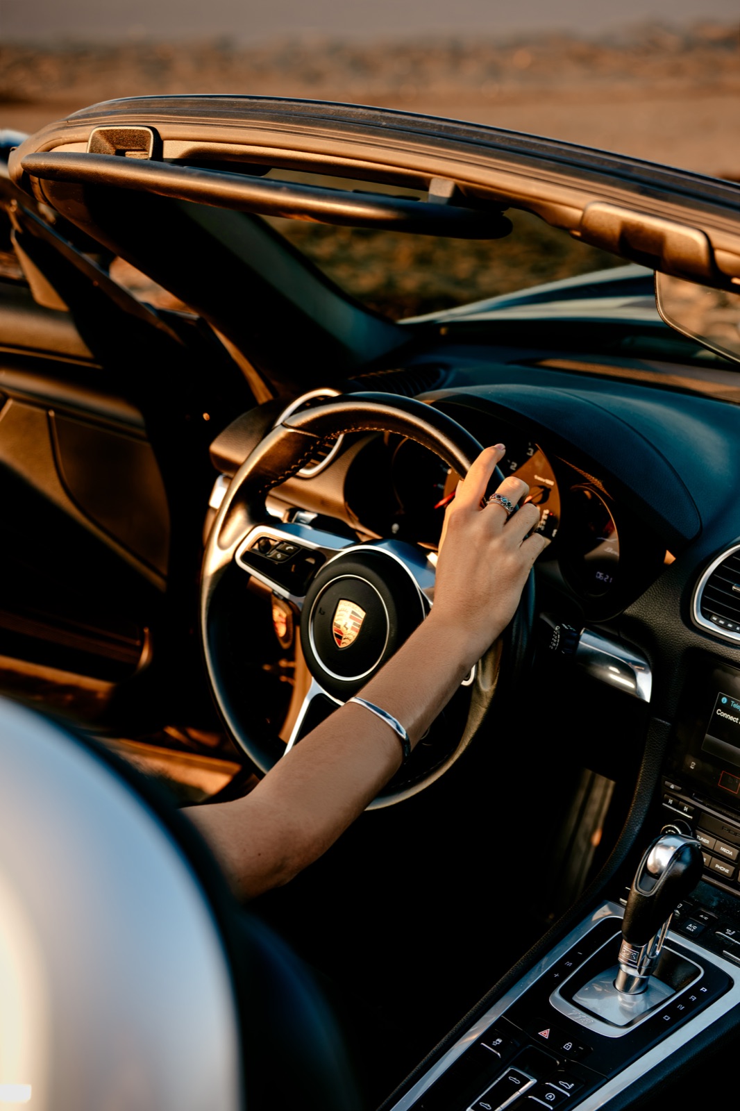 A driver's hand on the steering wheel of a convertible on an open road