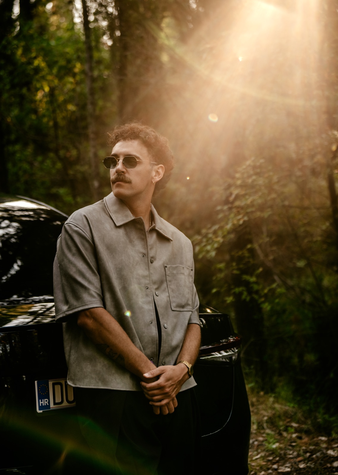 A man in sunglasses standing next to a rental car in a sunlit forest
