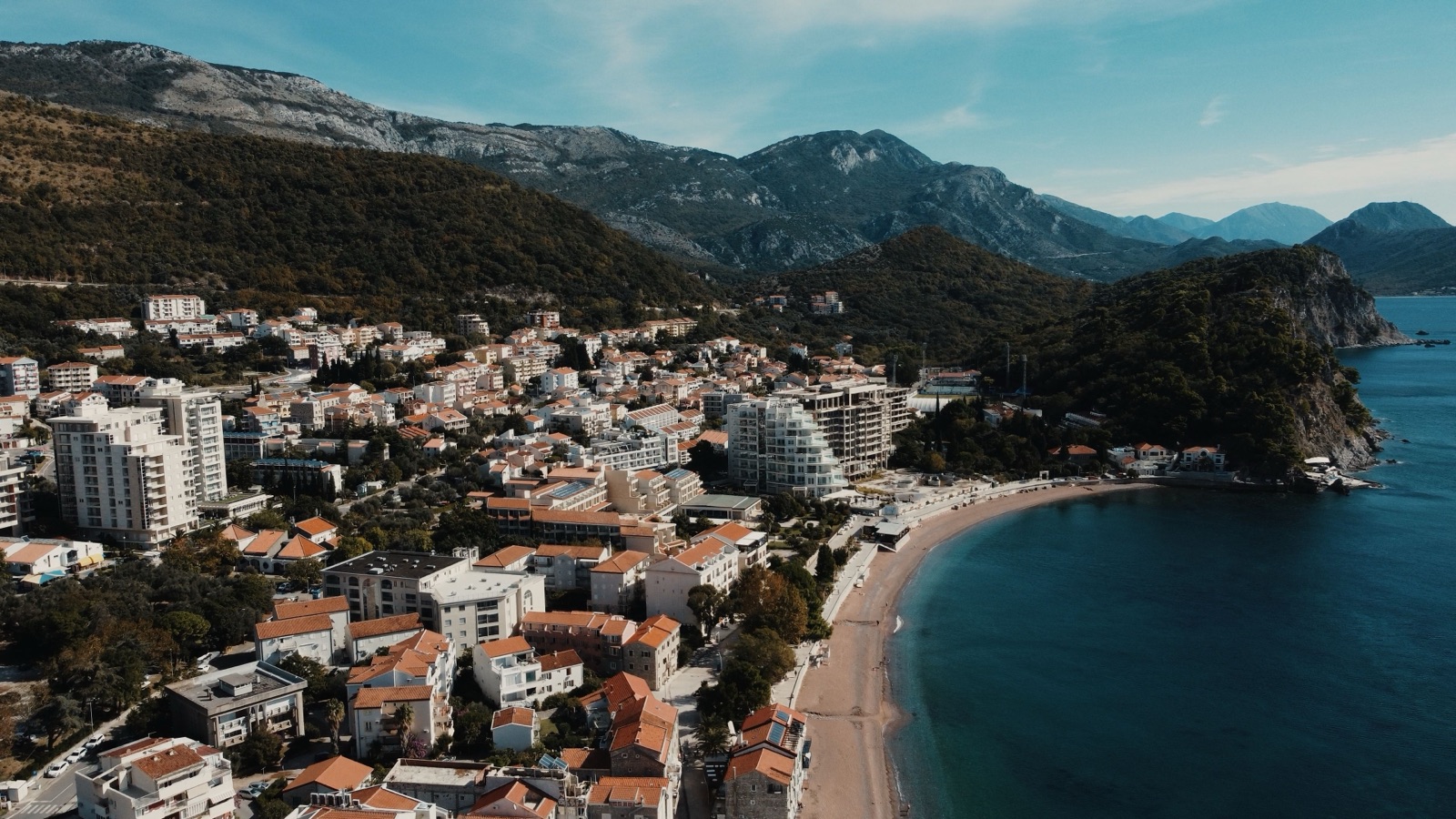 Aerial view of the Budva coastline with a long sandy beach, hotels and green hills