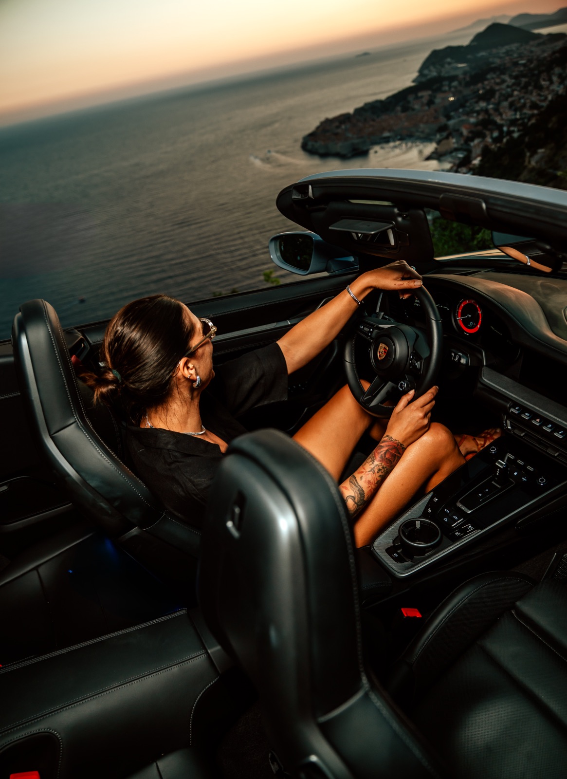 A woman driving a convertible along the coast above the Adriatic