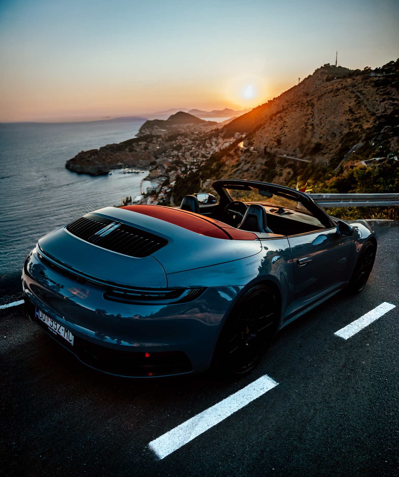 A convertible parked on a coastal road above Dubrovnik at sunset