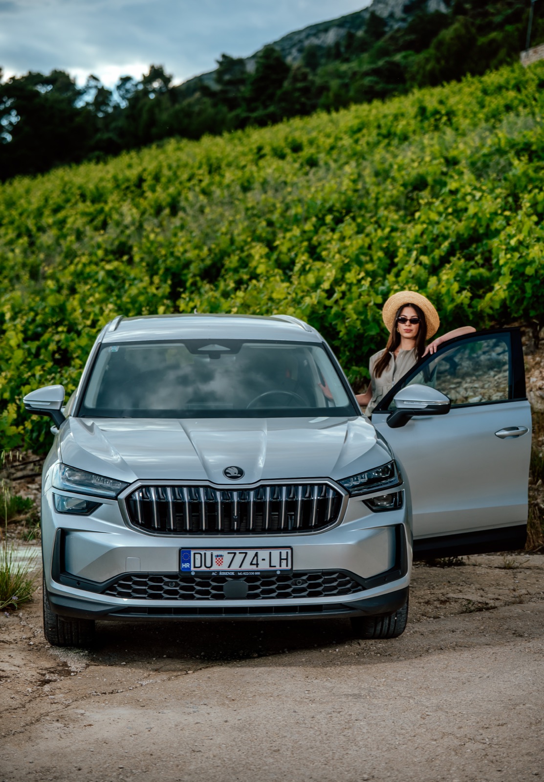 A woman standing by a silver Škoda SUV parked next to a vineyard on the Pelješac peninsula