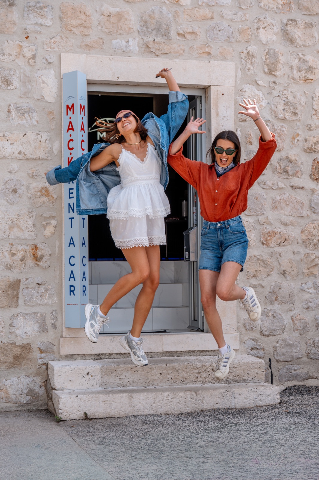 Two friends jumping for joy outside the stone doorway of the M.A.C.K. Rent a Car office