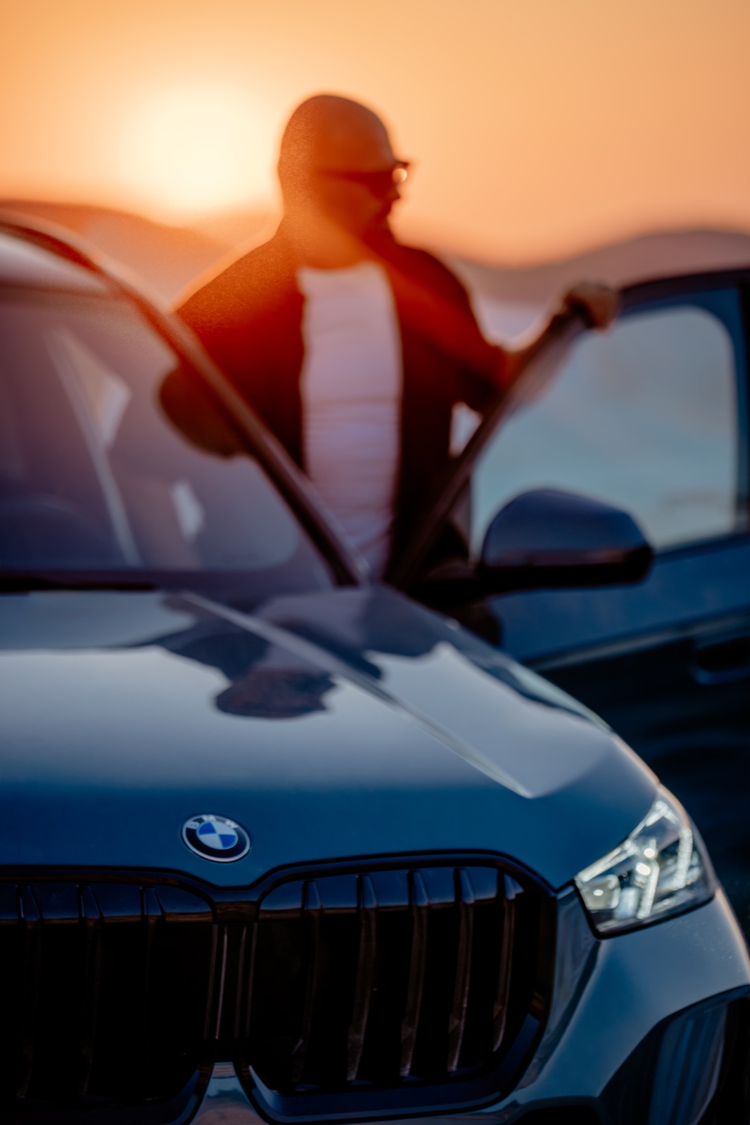 A man opening the door of a BMW rental car against the sunset