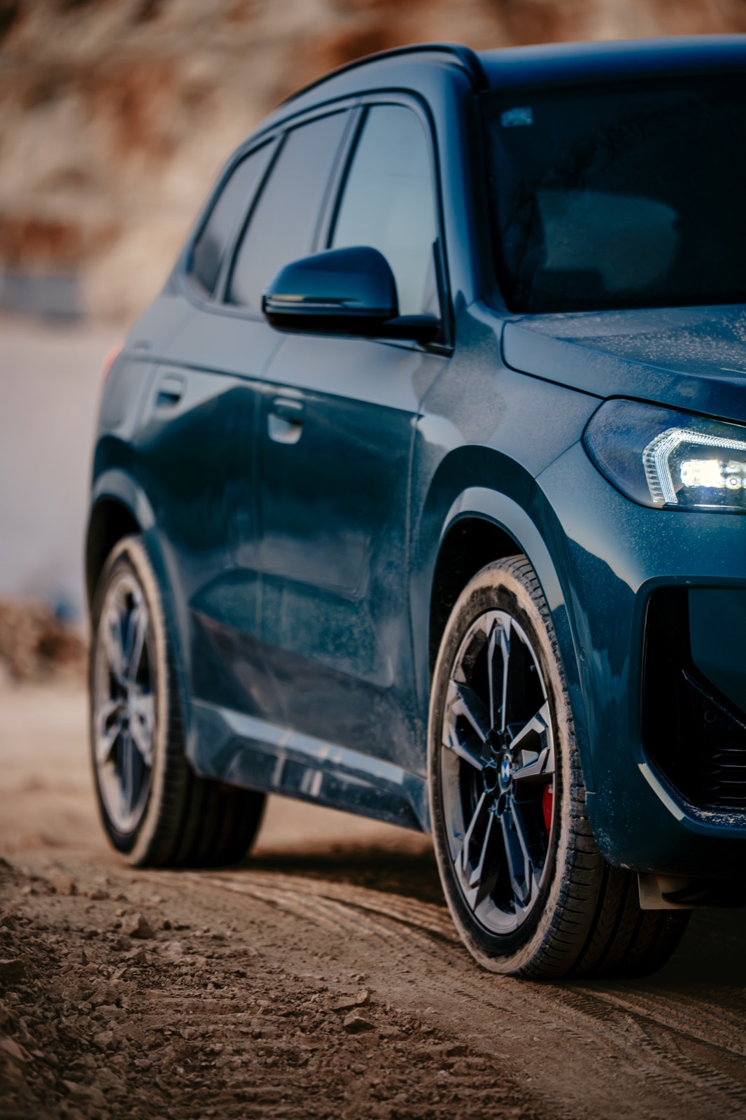 Close-up of a dark blue BMW X1 SUV on a dusty coastal road