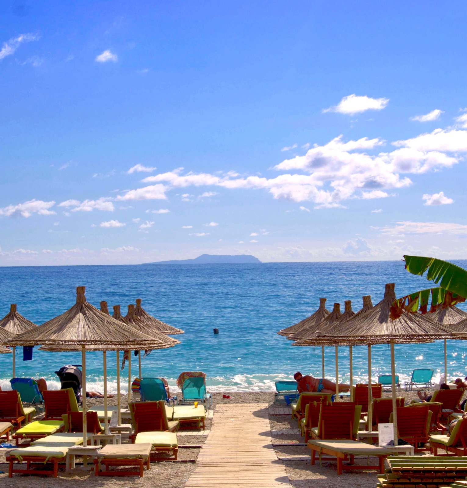 Straw parasols and sunloungers on an Albanian beach with clear blue sea