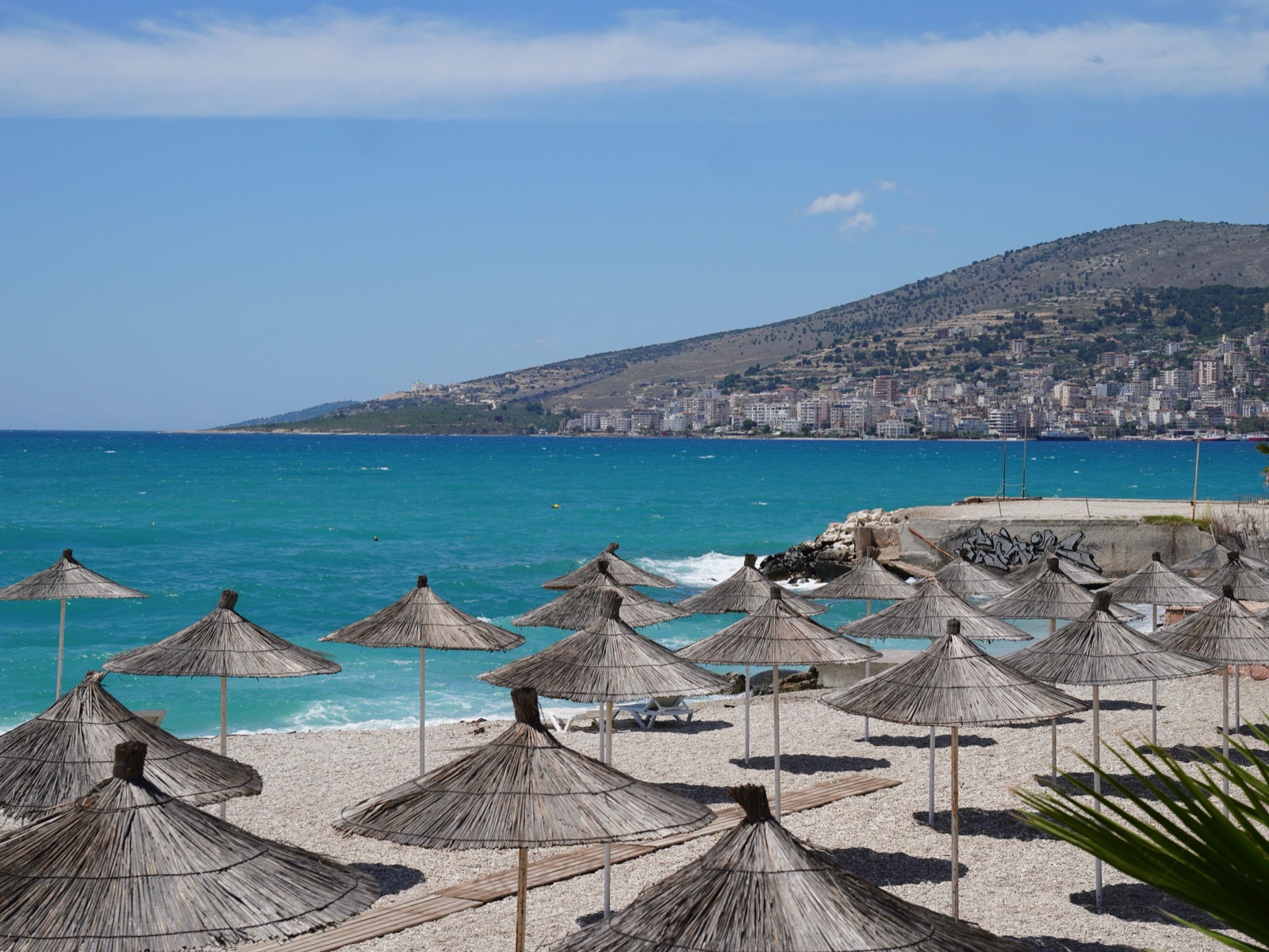 Rows of straw parasols on a pebble beach in front of the town of Sarandë