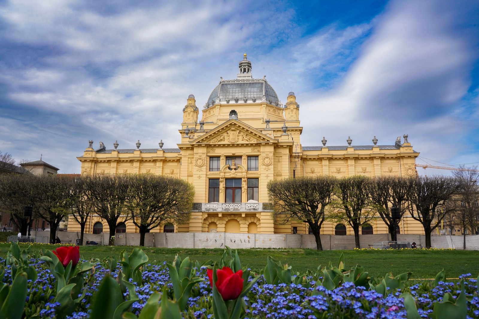 The yellow Art Pavilion in Zagreb behind a park with tulips in bloom