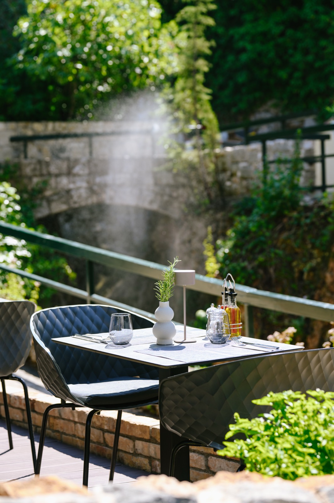 A set table on a shaded restaurant terrace above a stone bridge in Mlini